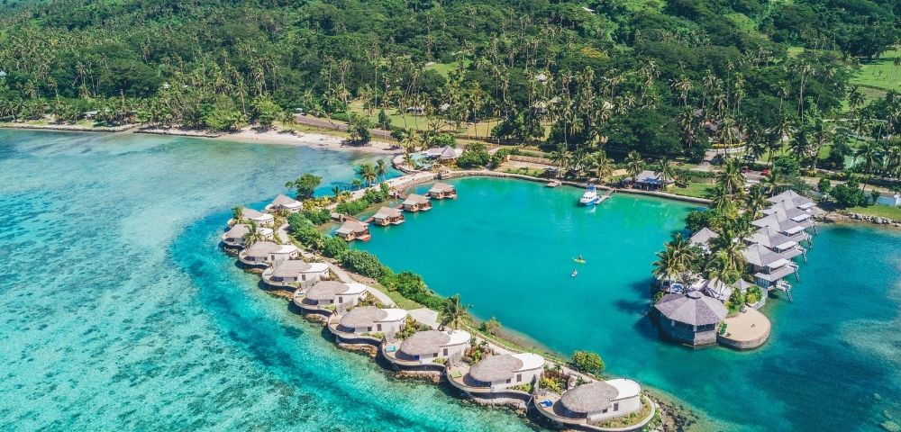 Aerial view of resort showing reef and over water villas with the lush jungle in the background