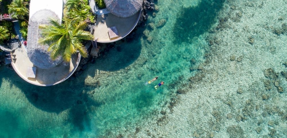 Aerial view of two people snorkelling over the reefs outside the resort rooms