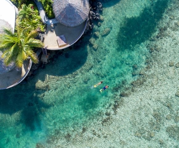 Aerial view of two people snorkelling over the reefs outside the resort rooms