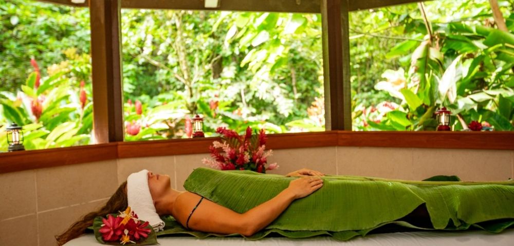 Woman relaxing in the spa wrapped in a banana leaf and towel over eyes with jungle in background