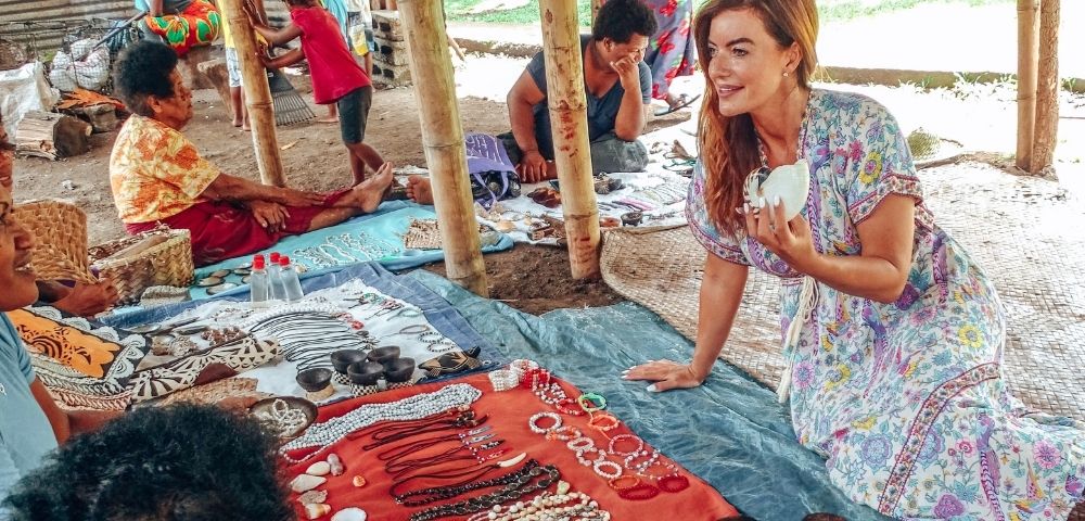 lady sitting with Fijian women discussing traditional crafts and jewellery displayed before her